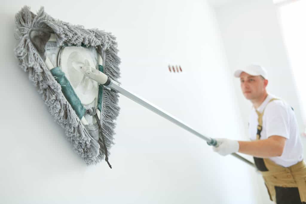 man cleans wall with mop